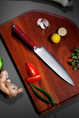 Professional Damascus steel chef knife on a wooden cutting board with fresh tomato, lemon, garlic,...