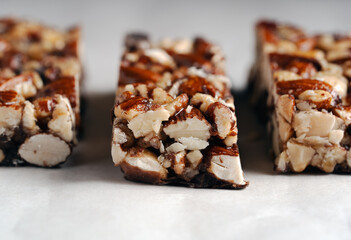 Low-angle close-up emphasizing the chunky texture and ingredients of three mixed nut bars on a light, clean surface