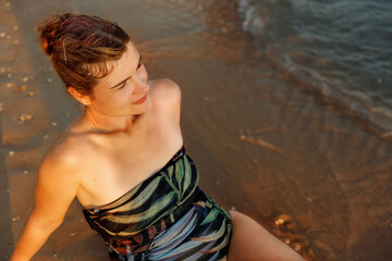 Fototapeta premium Portrait of a beautiful young woman relaxing on the sandy beach at sunset