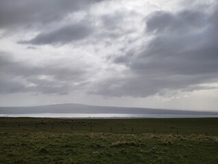 Green pasture with fence line overlooking bay under stormy sky Ireland