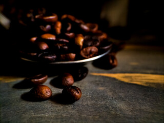 Dark roasted coffee beans spill from a metallic scoop onto a wooden surface.
