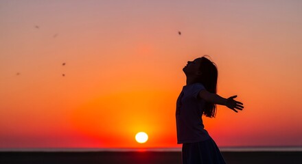 A young woman stands in a field at sunset with arms outstretched, embodying freedom and joy. This inspiring shot is perfect for wellness ads, travel blogs, or motivation projects.