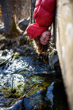 Side view of a young Boy in a puffer jacket hanging upside down over the edge of a bridge, USA