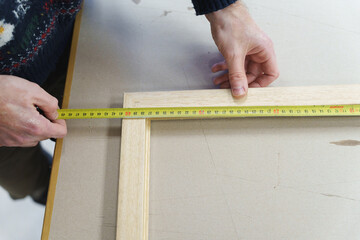 Hands of a technician using a yellow tape measure to check dimensions of a wooden frame.