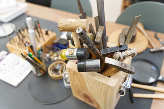 Various professional jewelry hammers and files stored in a wooden block on a workbench.