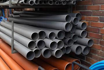 Stack of grey and orange PVC plastic pipes for sewage and plumbing drainage systems on a construction site.