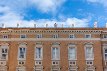 Neoclassical facade detail of the Royal Palace of Caserta with chimneys and windows under a blue sky, Italy © milan