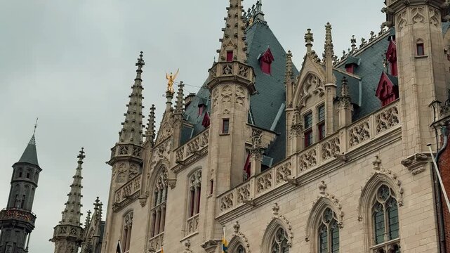 The stunning Burg Square in Bruges showcases its medieval history with a detailed white gothic building contrasting with brick architecture. A festive Christmas tree adds a touch of charm.

