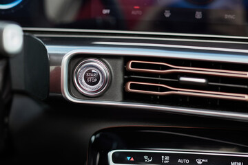 A close-up view inside a vehicle features the start/stop engine button and an air conditioning vent with copper colored trim detail.