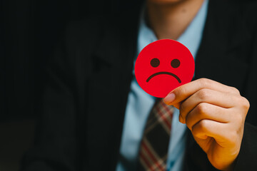 Feedback concept. Red unhappy face card held by person in business suit showing negative emotion and dissatisfaction in dark background
