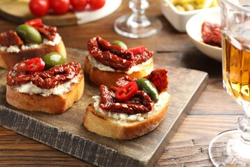 Delicious bruschettas with cream cheese, sun-dried tomatoes, chili pepper and green olives on wooden table, closeup