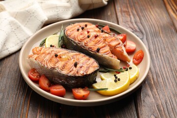 Tasty grilled salmon steaks served with lemon, rosemary and tomatoes on wooden table, closeup