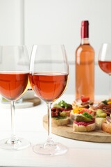Tasty bruschettas with prosciutto and rose wine served on white wooden table, closeup