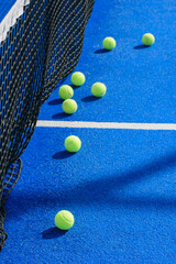Yellow padel balls scattered on a blue court next to the net The Concept of sport and leisure.