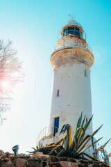 White lighthouse on a rocky coastline under clear blue sky with bright sunlight and mediterranean atmosphere. Paphos, Cyprus