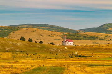 Small countryside church with red roof in golden rolling hills under soft sky, peaceful rural landscape symbolizing faith, hope, spirituality, solitude and harmony with nature