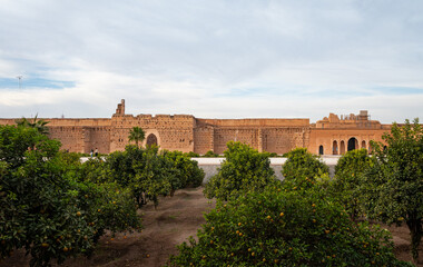 Fototapeta premium Ancient mud brick city wall with palm trees in Marrakech, Morocco. Traditional North African architecture with warm earthy tones and clear blue sky, ideal for travel, history, and background use.