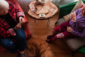 Overhead view of a Grandmother and her granddaughter sitting in a living room playing cards with dog lying on floor between them