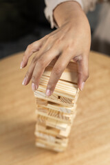 Obraz premium Close-up of a woman’s hand carefully placing a wooden block on top of a fragile stacking tower during a tense tabletop game focused on balance, precision, and control.
