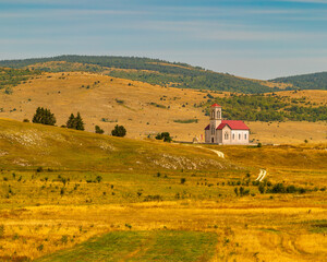 Lonely countryside church with red roof in golden rolling hills, peaceful rural vertical landscape with copy space, symbolizing faith, spirituality, silence, hope, travel inspiration and harmony with 