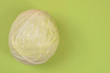 A whole fresh head of white cabbage with pale green leaves placed on a matching light green surface