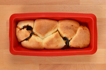Freshly baked sweet buns filled with dark plum jam are nestled together in a red silicone mold on a wooden table