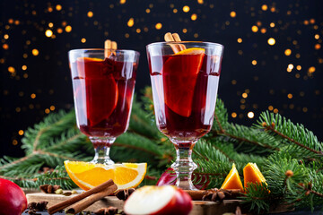Mulled wine. Festive drinks served in elegant glasses, garnished with fruits and spices, placed on wooden table surrounded by Christmas tree branches, creating warm and inviting holiday atmosphere