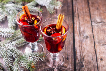 Mulled wine. Festive holiday drinks served in elegant glasses, garnished with spices and fruits, placed on rustic wooden table surrounded by evergreen branches, creating warm and inviting atmosphere