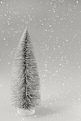 Artificial Christmas tree on Gray background with falling snow. Festive background with copy space. Vertically. Demonstrating color of 2026 year, Cloud, Dancer