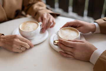 Coffee hands date couple holding warm cappuccino cups on white table in cozy cafe