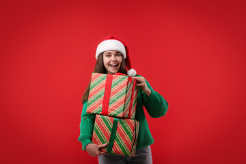 Fototapeta premium Beautiful woman in Santa hat with Christmas gifts on red background. Space for text