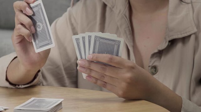 Woman holding playing cards at a table during a casual card game, focusing on strategy, leisure, and social entertainment at home.