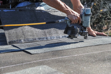close up on handyman using nail gun to install shingle to repair roof