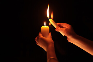 Hands holding burning candle in black dark. Selective soft focus, blur smoke light and shadow contrast background.