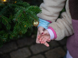 Child's hands with red nail polish holding a golden Christmas bauble 