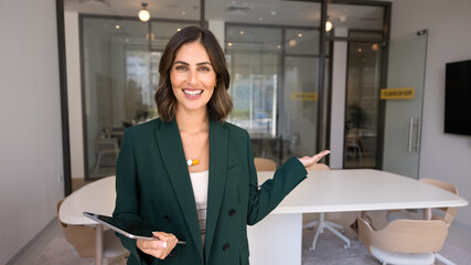 Happy young professional woman pointing hand at modern office interior, looking at camera for portrait, presenting workspace, welcoming onboard, offering job, hiring, business space for rent © fizkes