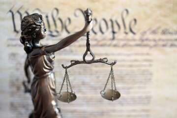 The statue of justice Themis, the blindfolded goddess of justice against US Constitution page. Judgement and punishment in United States