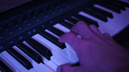 Close-up view of a single hand pressing keys on a digital synthesizer keyboard illuminated by vibrant RGB lights. The continuously changing colors add visual energy to the music.