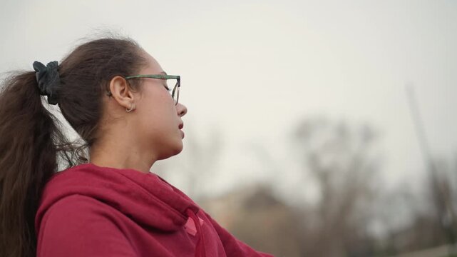 Focused Woman Stretching Outdoors, Asian Woman Engaged In Mindful Stretching Under Cloudy Sky, Tranquil Female Performing Controlled Breathing And Gentle Stretches Amidst City Greenery