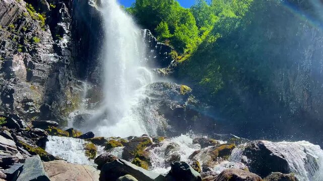 Dombai-Ulgen Gorge, Chuchhur waterfall is framed by malachite greenery of grasses and dense forests. A waterfall flowing down from a glacier. A two-stage stream with white foam, near the Chuchhur pass