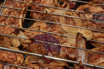 Juicy pieces of chicken are grilled in a metal grill over hot coals. The ruddy crust and smoky...
