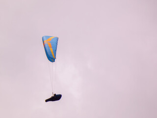 A blue paraglider soaring in the cloudy sky