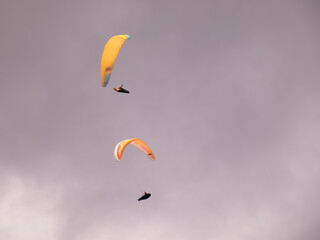 A pair of colorful paragliders in a cloudy sky