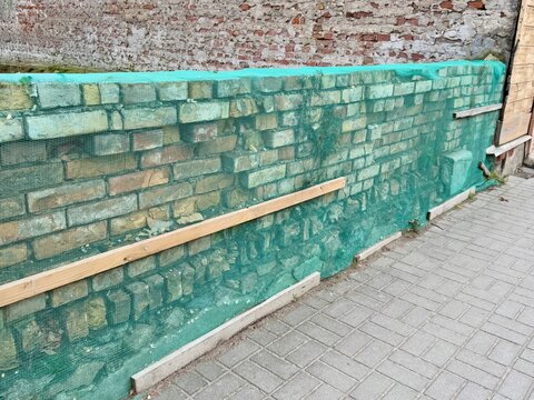 Brick wall with green waterproofing membrane applied during building renovation, showing foundation insulation, moisture protection, and construction work in progress.