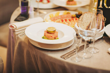 A table is set with glasses and plates of food during a dining event. There are dishes with meat, seafood, and bread, showing a variety of options for guests to enjoy