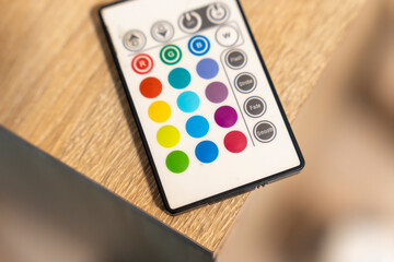 A colorful LED remote control is placed on a wooden surface, showing various color buttons for...