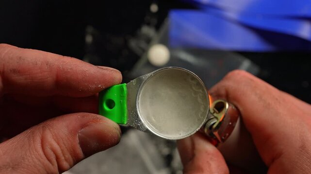 Drug user preparing liquid drugs in the tin cooker container used for mixing and heating a drug with lighter. Drug such as cocaine, white heroin or crack cocaine mixed and dissolved with water.