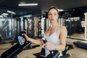 Fototapeta premium Young fit woman preparing for a workout on a dip station machine in a modern gym, focused and ready for strength training.