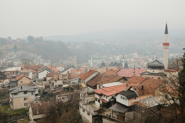 Fototapeta premium Foggy panoramic view of Travnik city in Bosnia and Herzegovina with traditional houses and mosque minaret seen from Travnik Fortress.