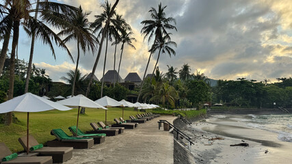 Row of white umbrellas and lounge chairs in front of the beach and the sea in Bali, Indonesia